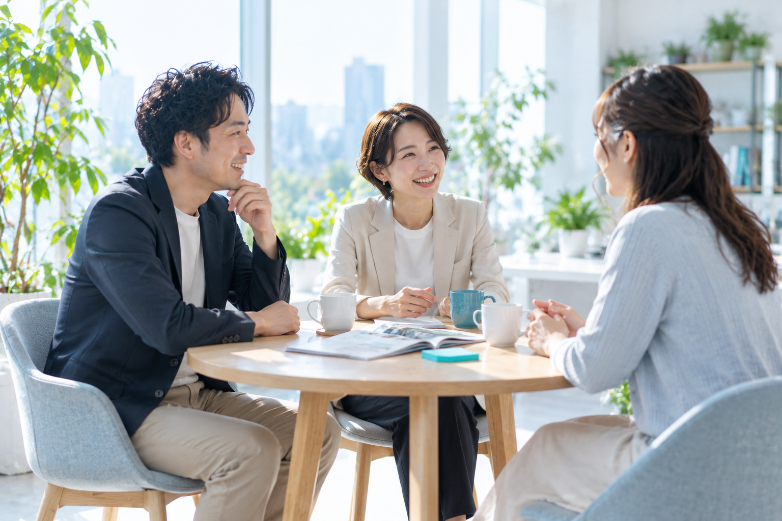 窓際の丸いテーブルで、会社の2人と応募者が笑顔で話しているカジュアル面談(AIで作成したイメージ)